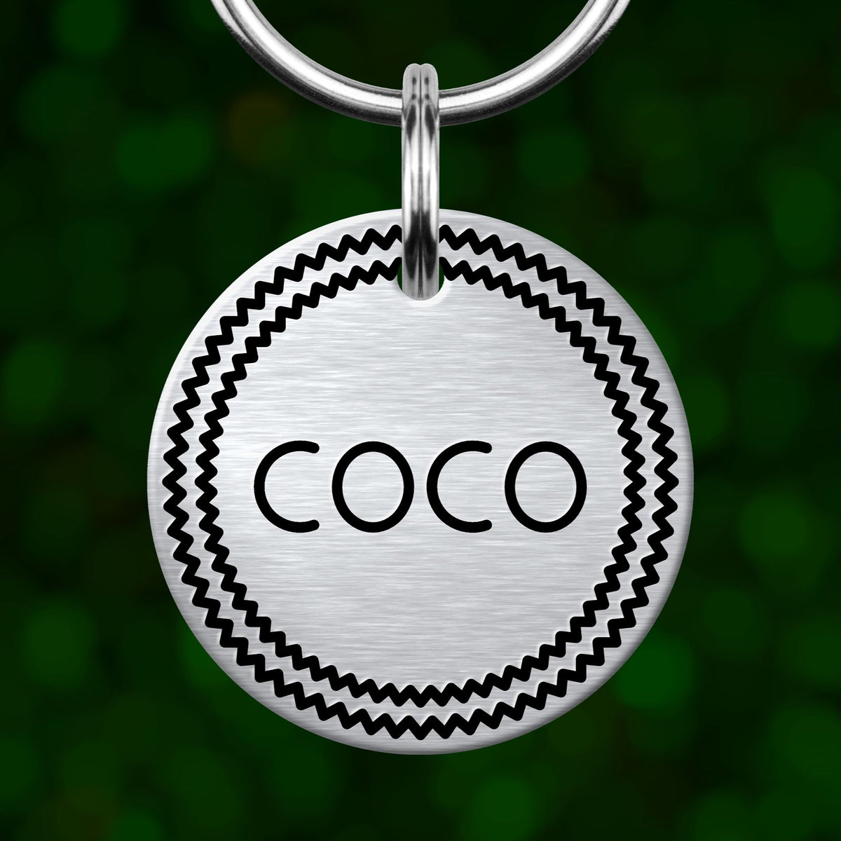 A silver-colored metal tag with the word "COCO" printed on it, hanging from a keychain.