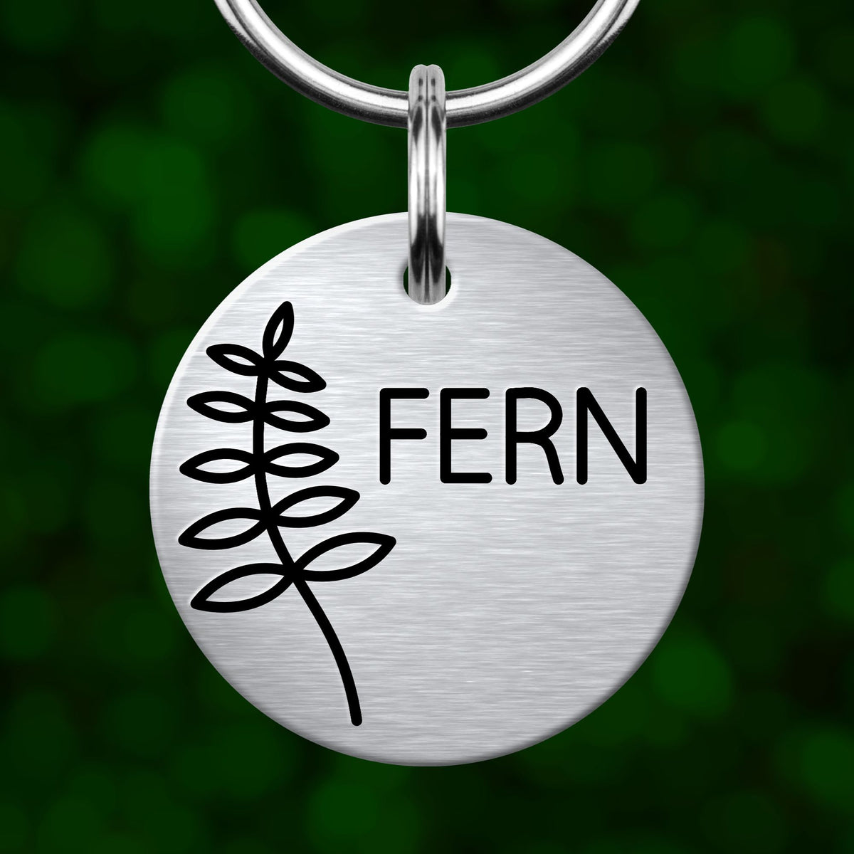 A round metal keychain with the word "FERN" printed on it, set against a blurred green background.