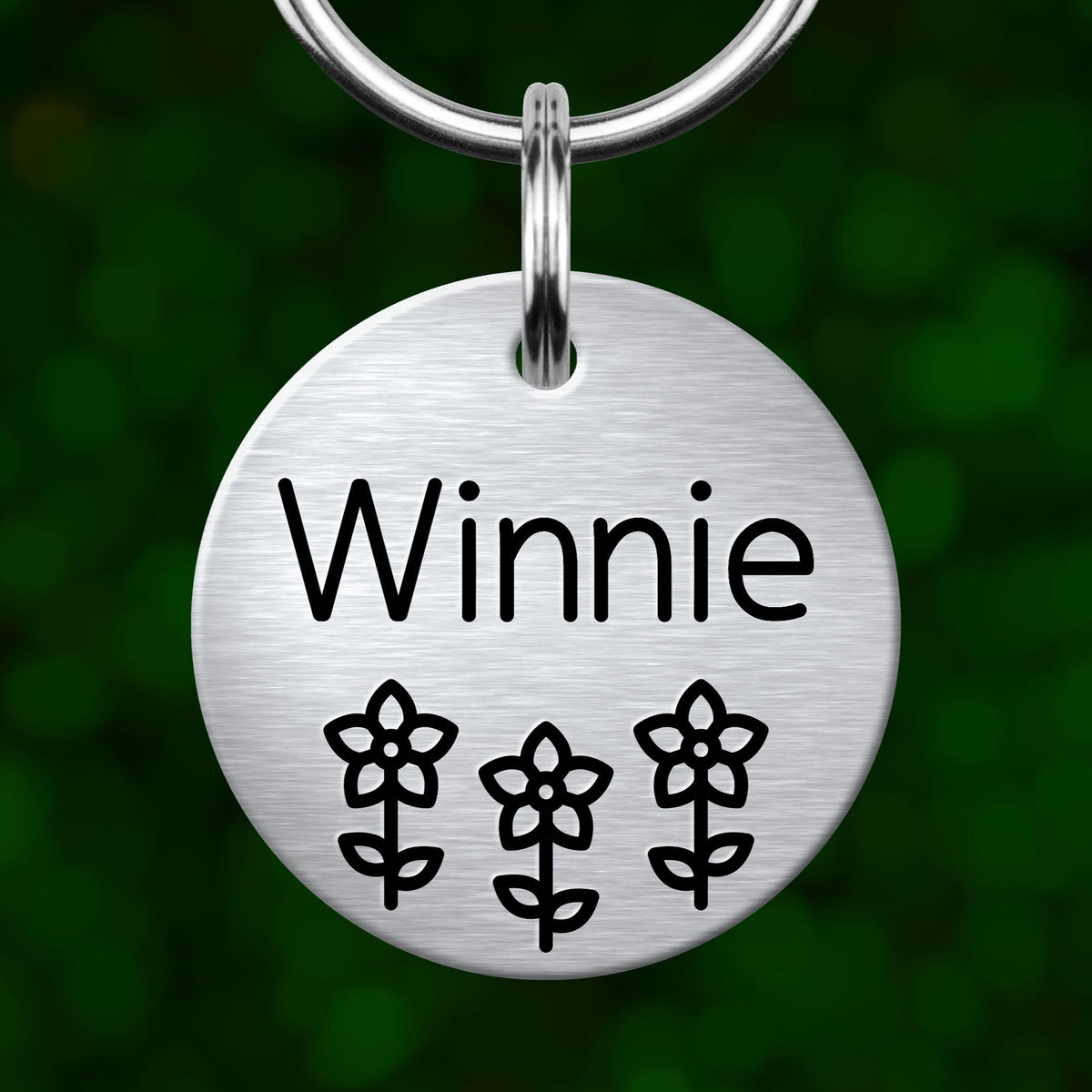 A round metal pet tag with the name "Winnie" and three flower icons printed on it.