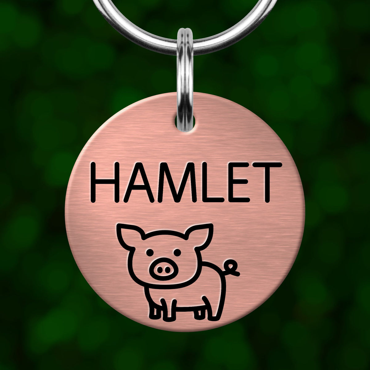 A round metal pet tag with the name "HAMLET" printed on it, featuring a simple cartoon pig illustration.