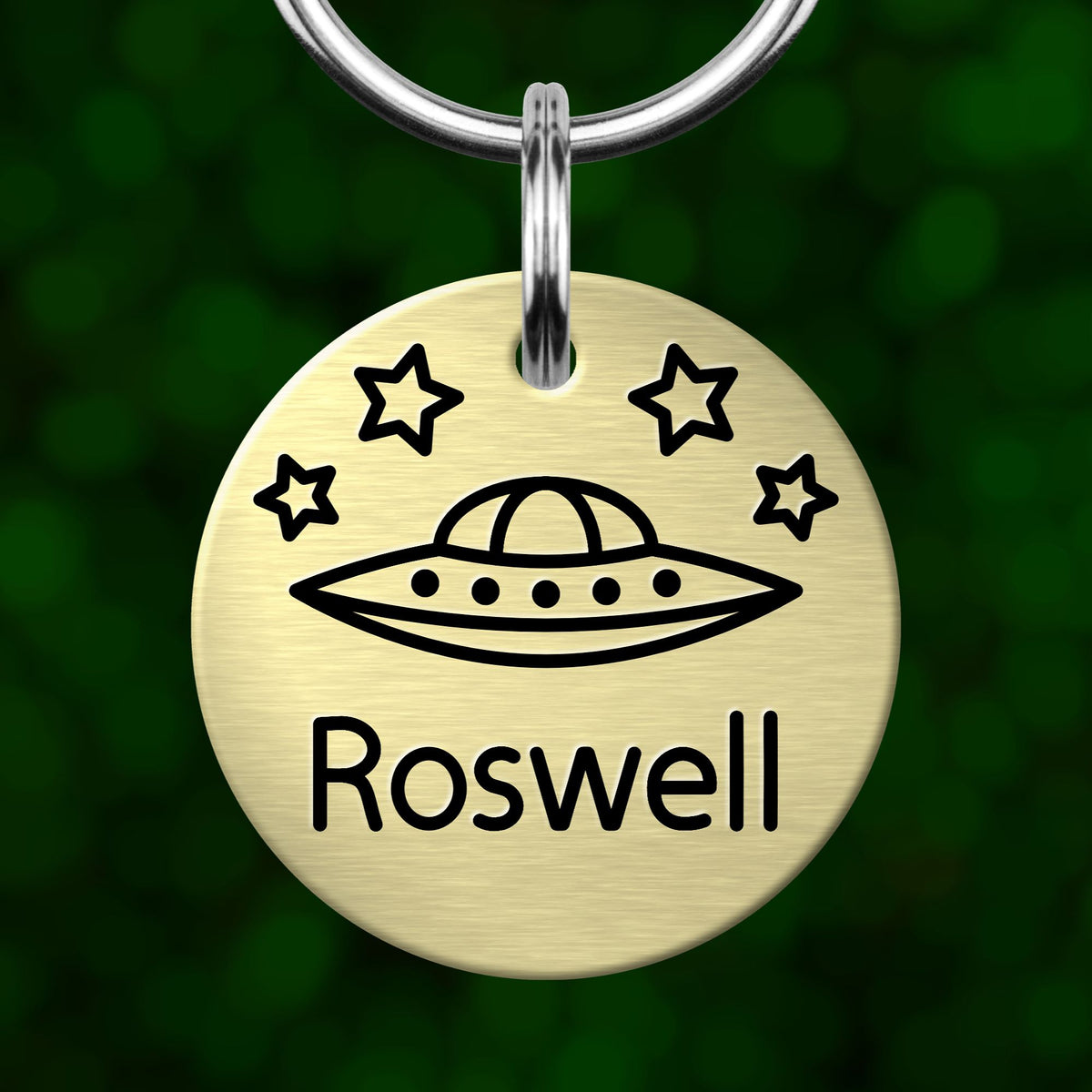 A round metal keychain tag with a graphic of an alien spacecraft and stars, and the name "Rosa" written on it.