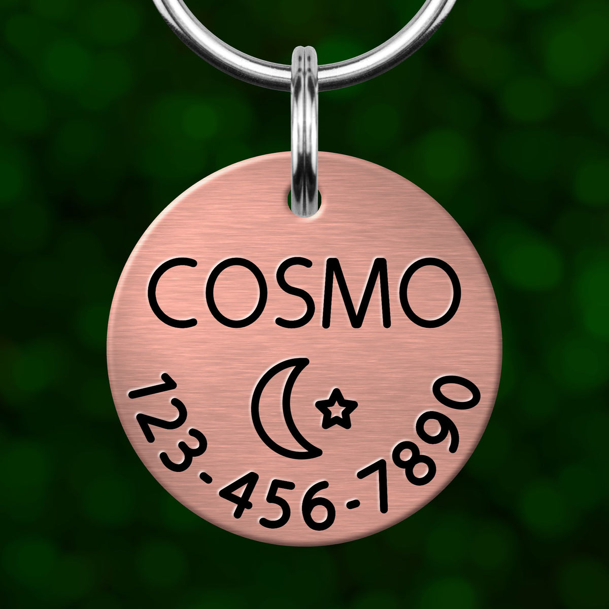A copper-colored pet name tag with the name "COSMO" and a phone number "123-456-7890" printed on it.