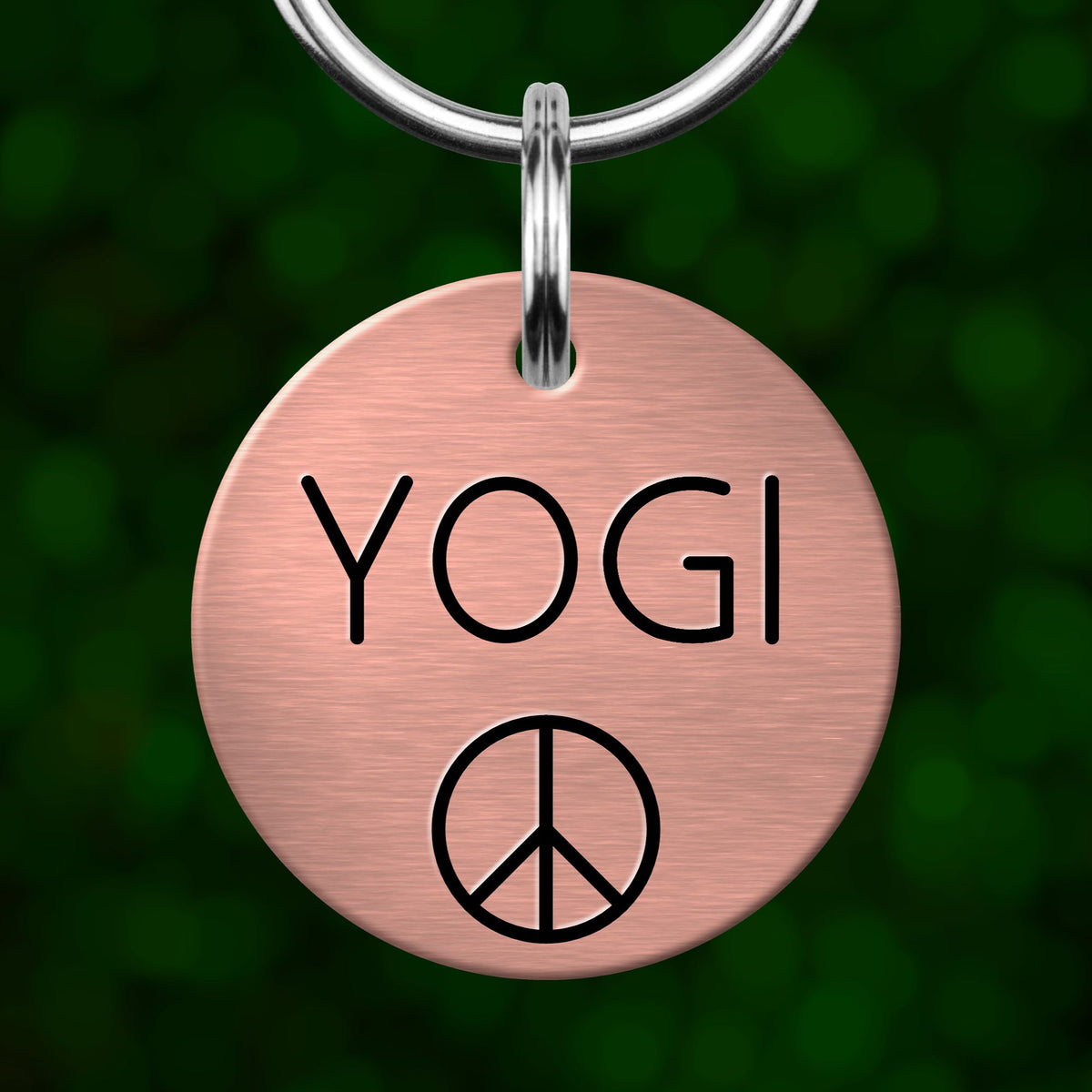 A pink circular pet tag with the word "YOGI" and a peace symbol printed on it.