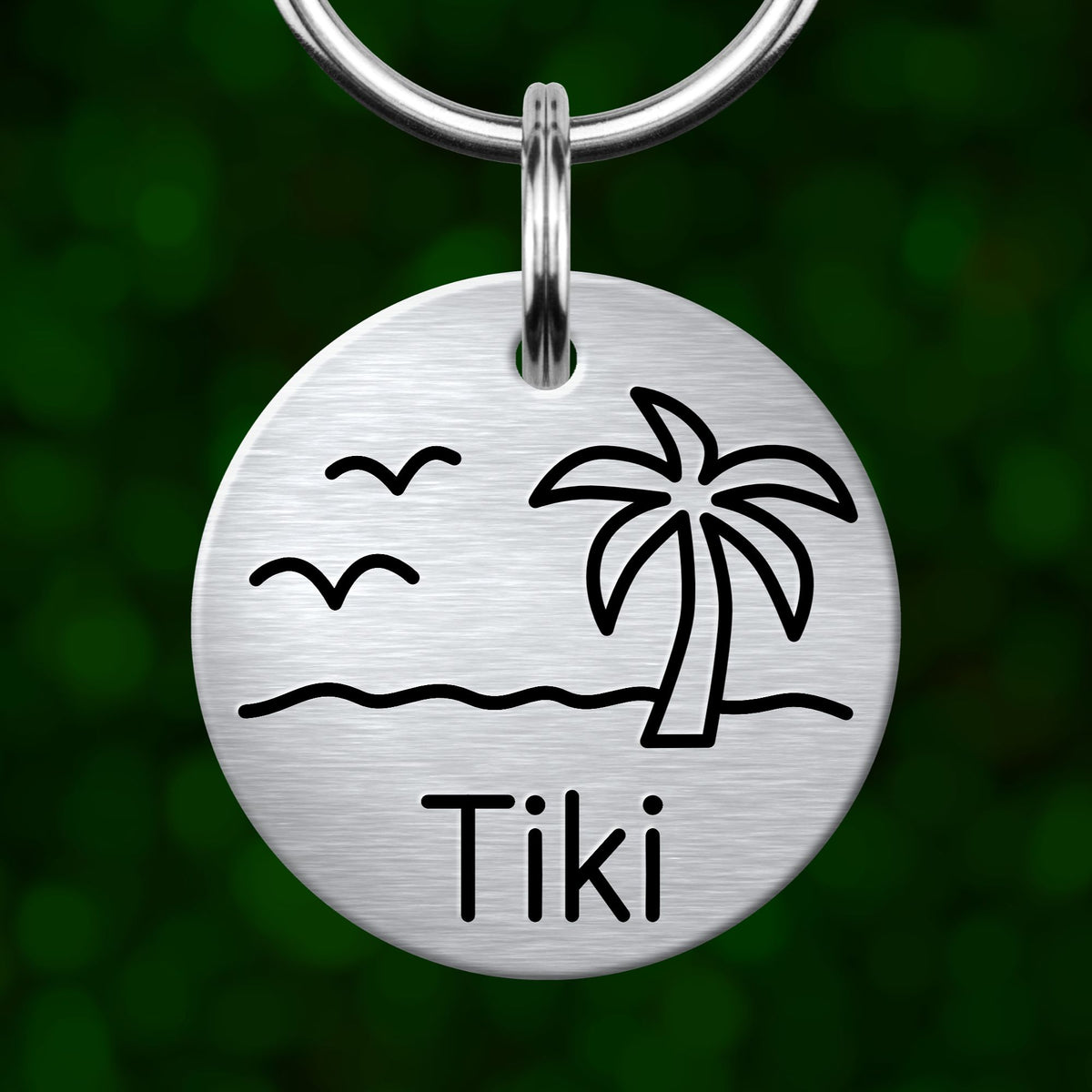 A round metal keychain with a design of a palm tree and birds, along with the name "Tiki" written below it.