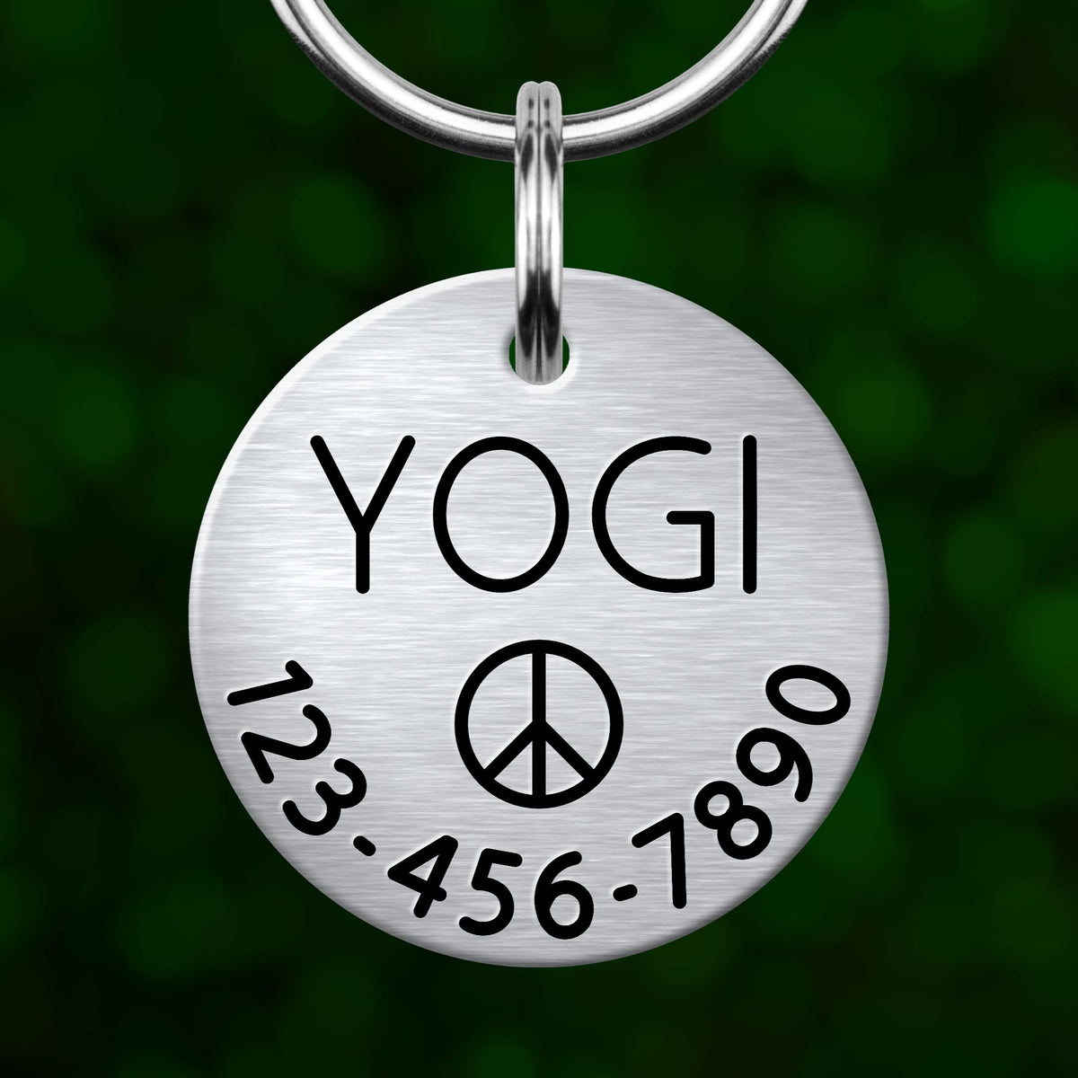 A silver-colored metal pet tag with the word "YOGI" printed on it, along with a peace symbol and a phone number.