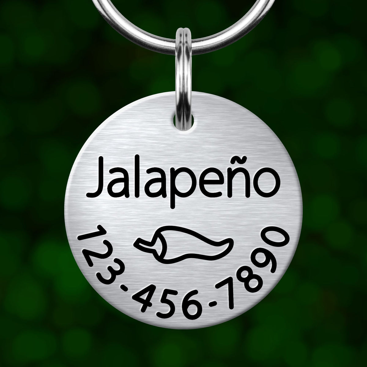 A silver-colored metal pet tag with the word "Jalapeño" printed on it, along with a chili pepper icon and a phone number.