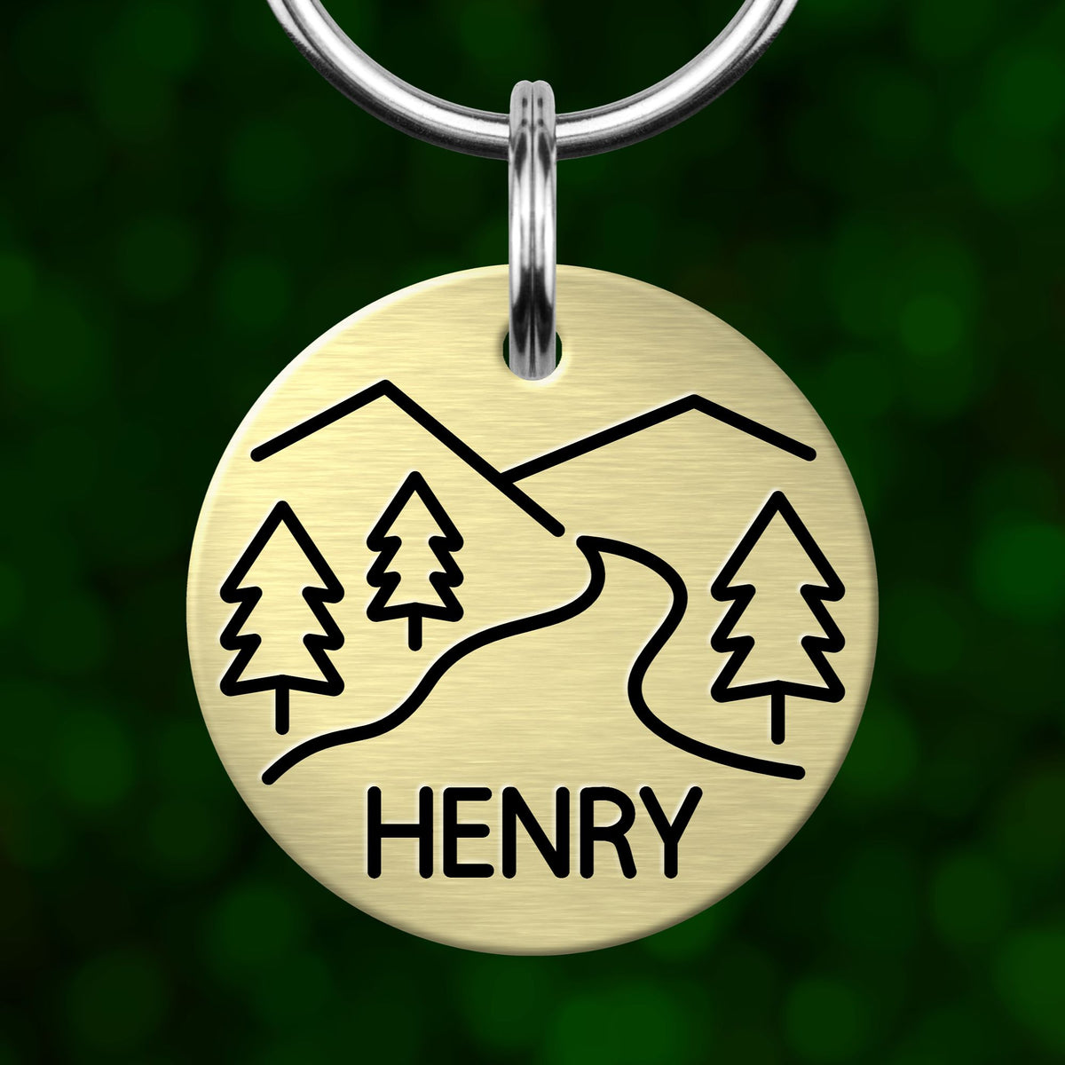 A round metal keychain with a design of trees and a winding road, and the name "HENRY" written below it.
