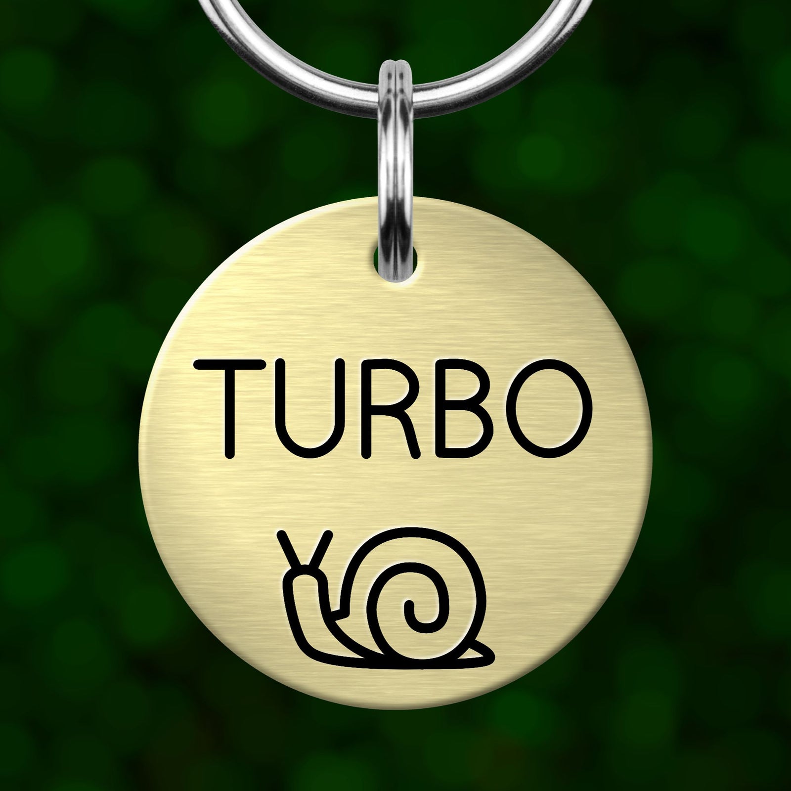 A round metal pet tag with the word "TURBO" printed on it, featuring a simple black and white illustration of a snail.