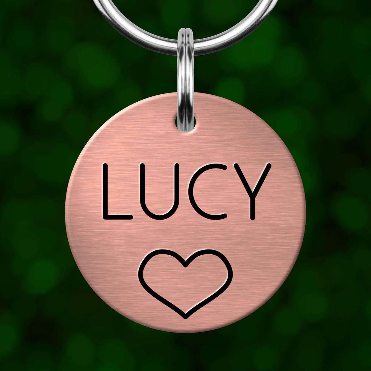 A pink metal pet tag with the name "LUCY" and a heart symbol printed on it.