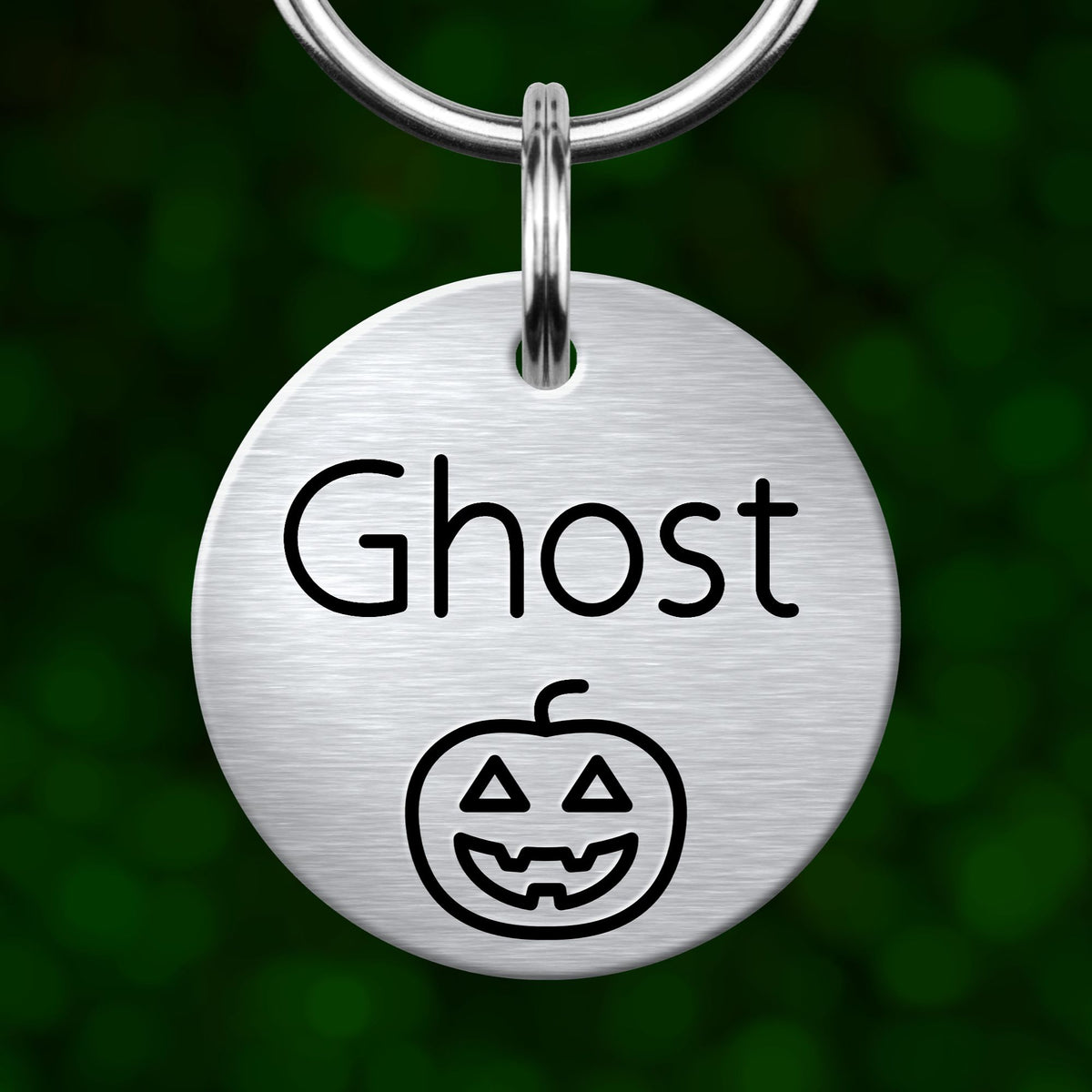 A round metal dog tag with the word "Ghost" and a pumpkin icon printed on it, hanging from a keychain.