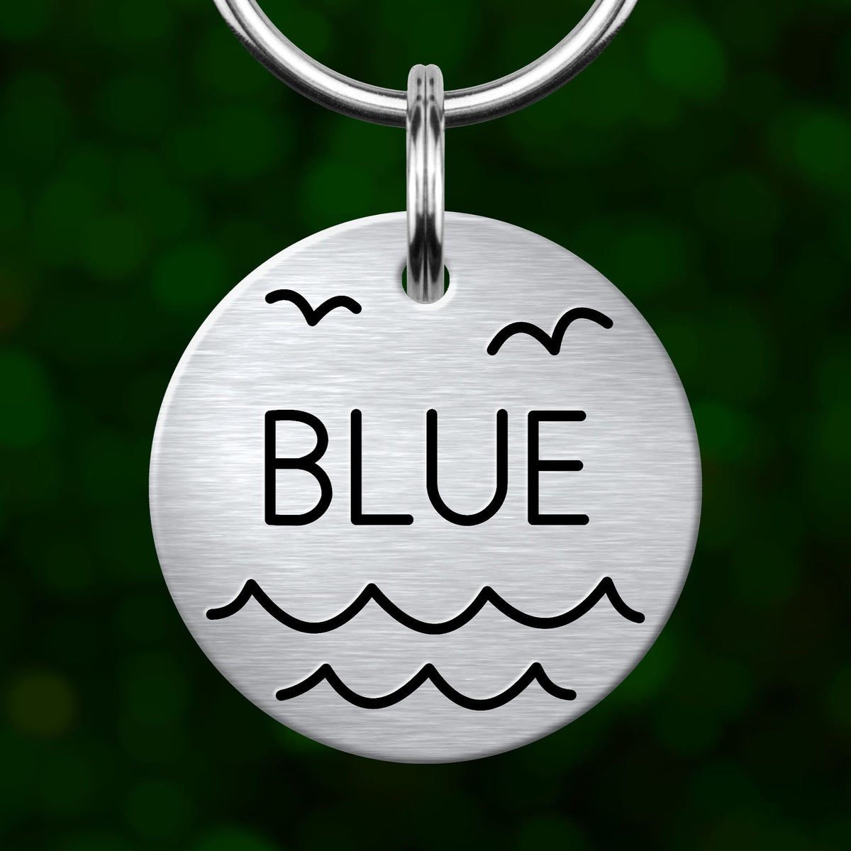 A round metal keychain tag with the word "BLUE" printed on it, featuring a wave and bird design.