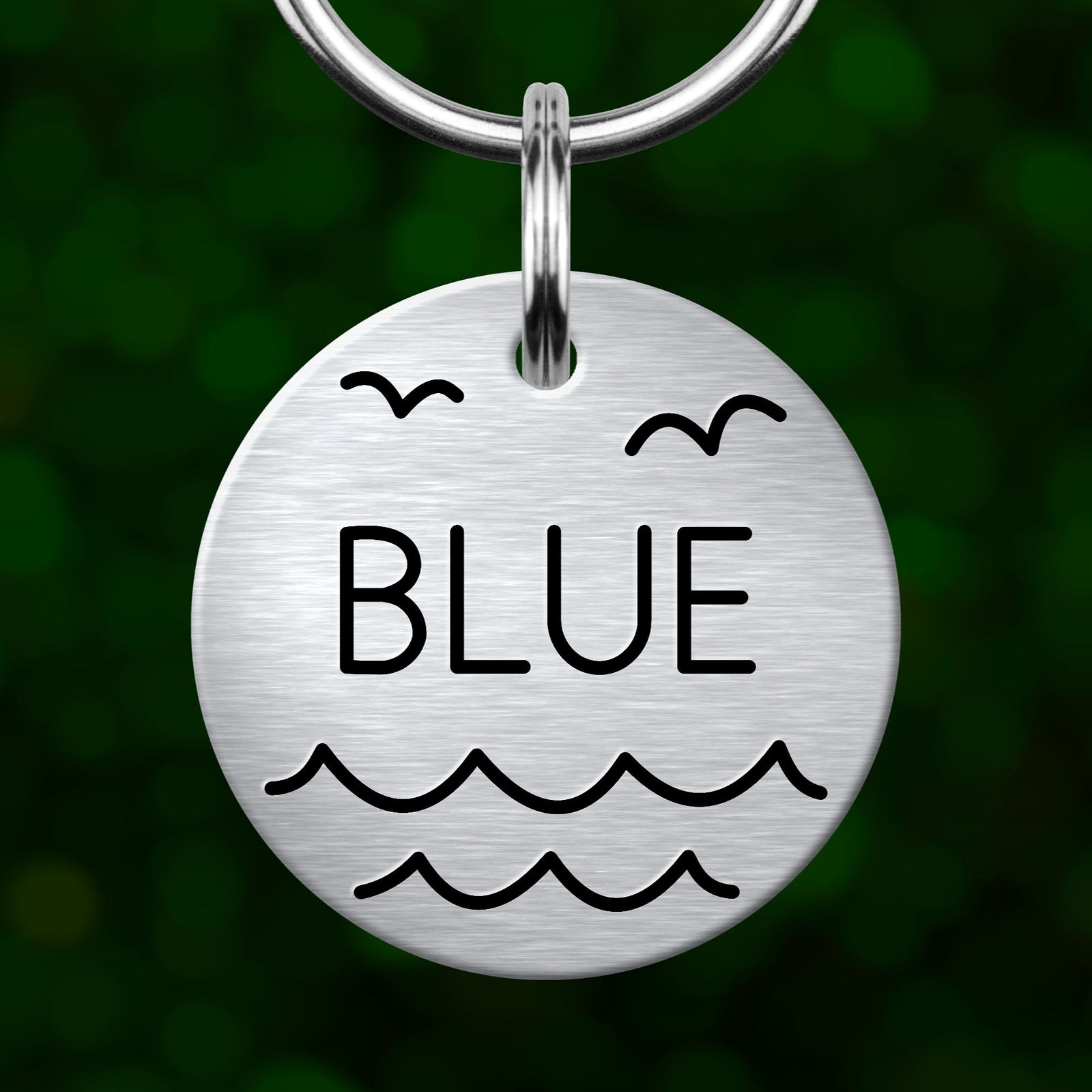 A round metal keychain tag with the word "BLUE" printed on it, featuring a wave and bird design.