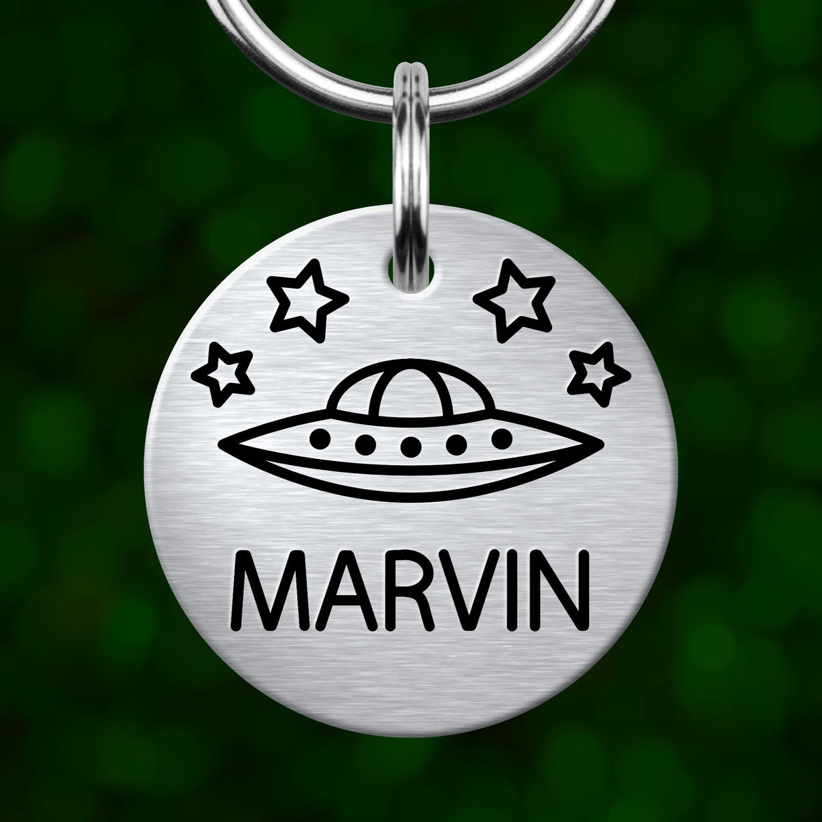 A silver circular pet tag with a graphic of an alien spacecraft and stars, and the name "MARVIN" printed below it.