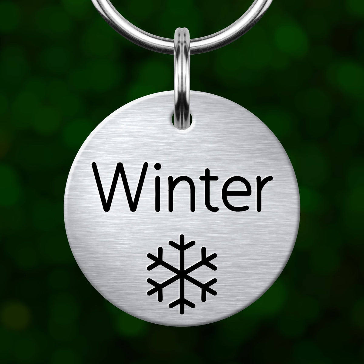 A round metal keychain tag with the word "Winter" written on it, along with a snowflake symbol.