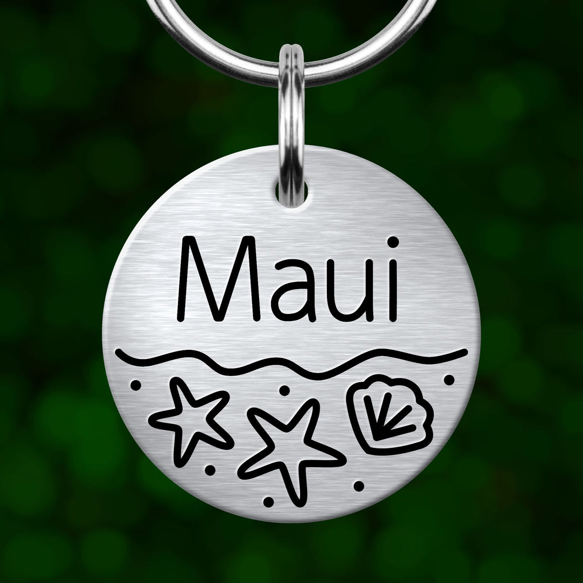 A silver circular pet tag with the name "Maui" written on it, along with two starfish and a seashell design.