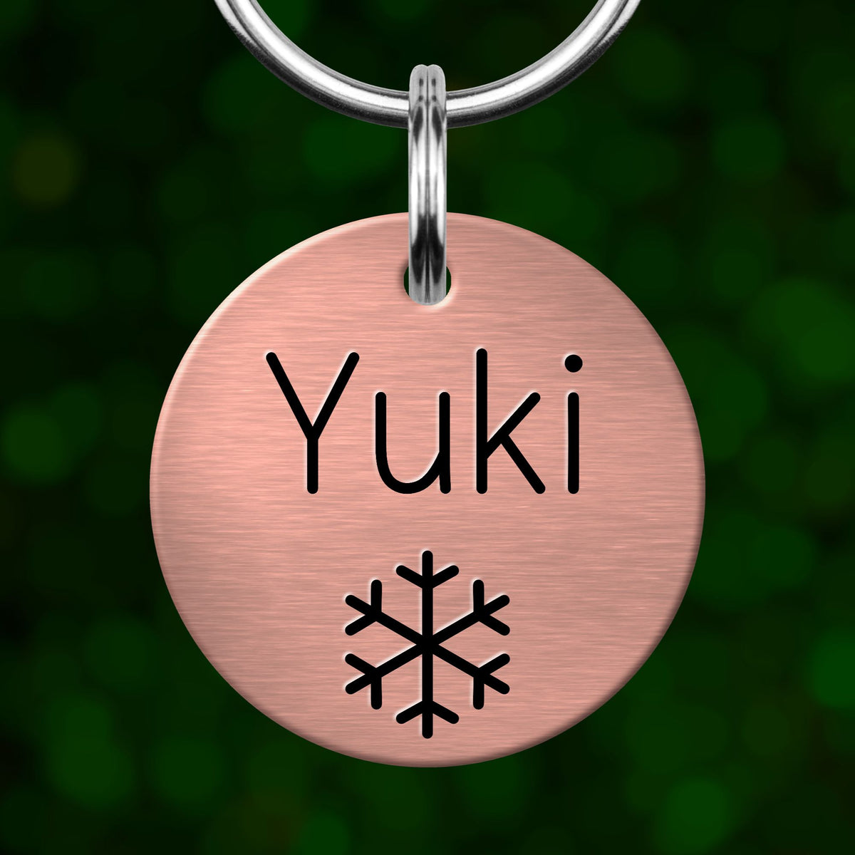 A round metal pet tag with the name "Yuki" printed on it, with a snowflake symbol below the text.