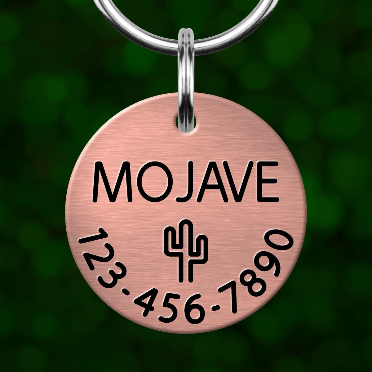 A copper-colored metal pet tag with the name "MOJASE" and a phone number "123-456-7890" printed on it.
