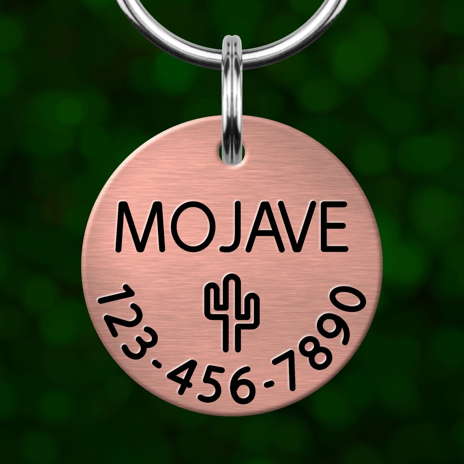 A copper-colored metal pet tag with the name "MOJASE" and a phone number "123-456-7890" printed on it.