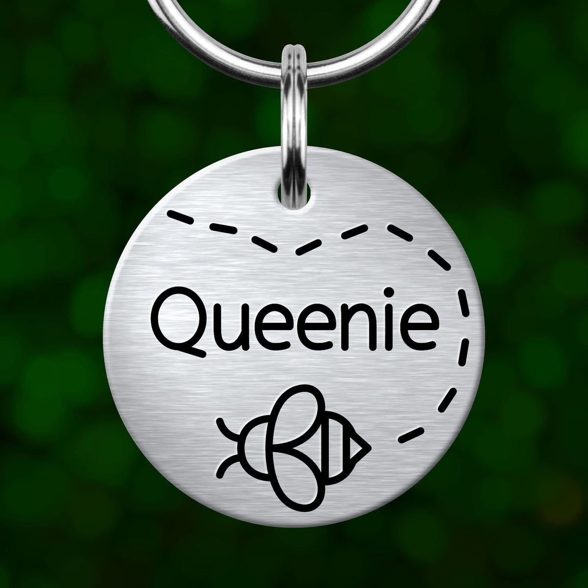 A round metal keychain tag with the name "Queenie" printed on it, featuring a bee symbol.