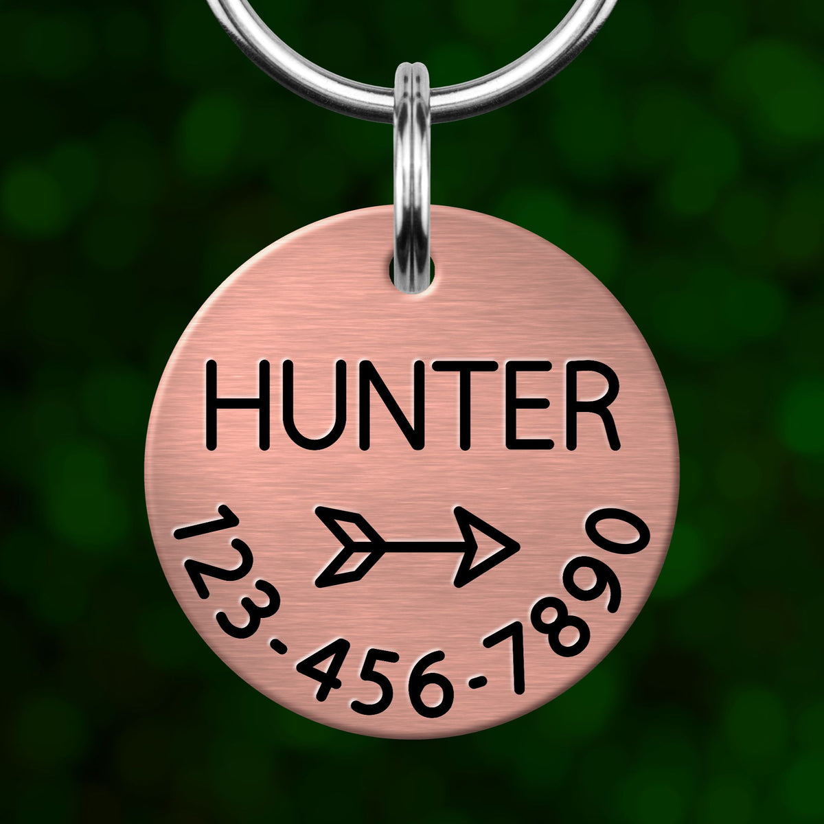 A copper-colored metal tag with the name "Hunter" and a phone number on it, hanging from a keychain.
