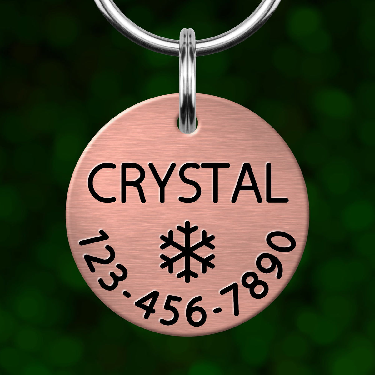 A copper-colored pet tag with the name "CRYSTAL" and a snowflake symbol, along with the numbers "123-456-7890".