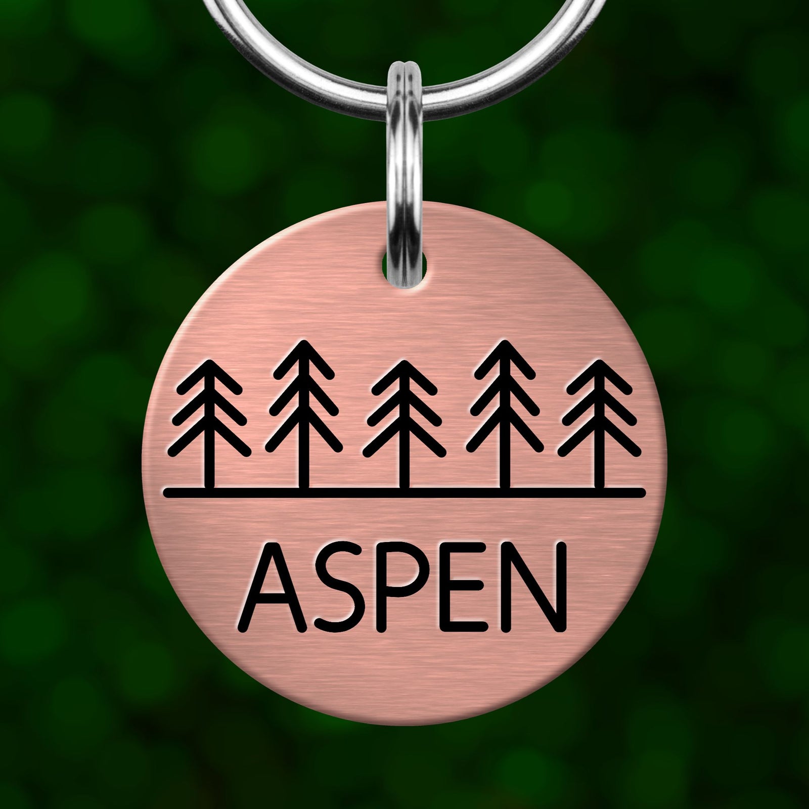 A round metal pet tag with a design of trees and the word "Aspen" printed on it.