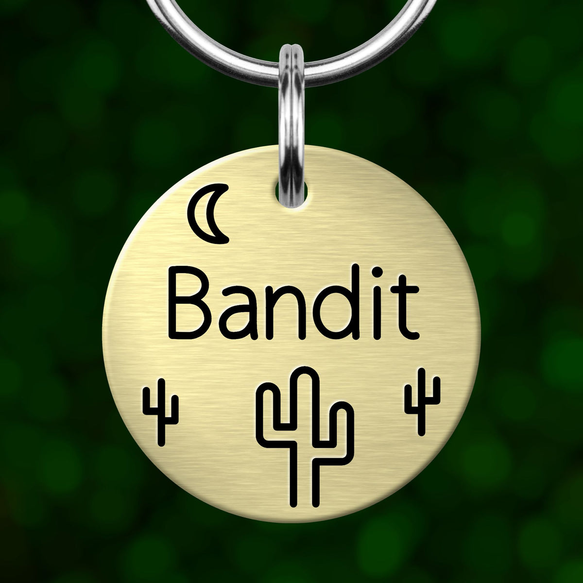 A round metal keychain tag with the word "Bandit" written on it, along with a cactus symbol and a crescent moon.