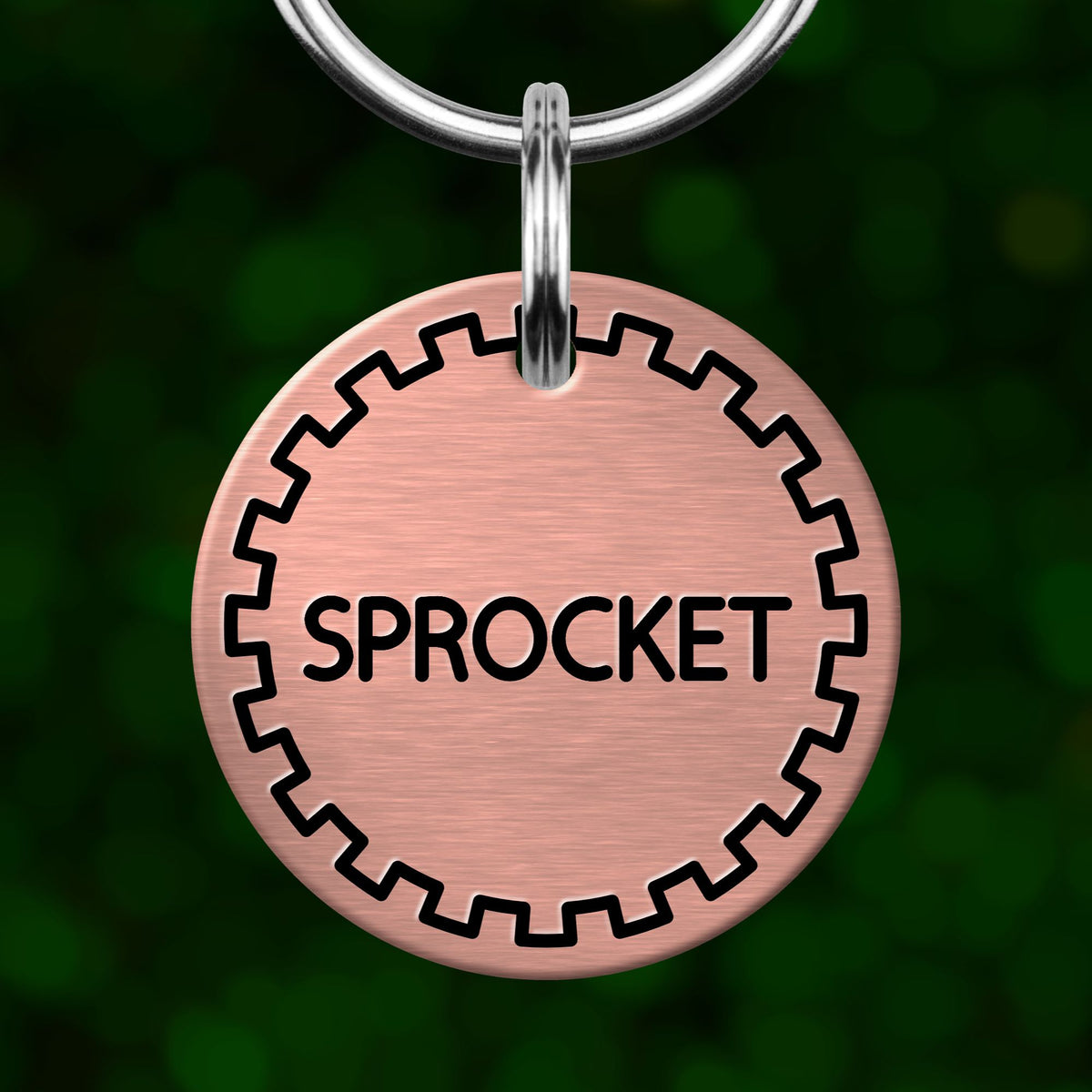 A round, metallic dog tag with the word "SPROCKET" printed on it, hanging from a metal loop.