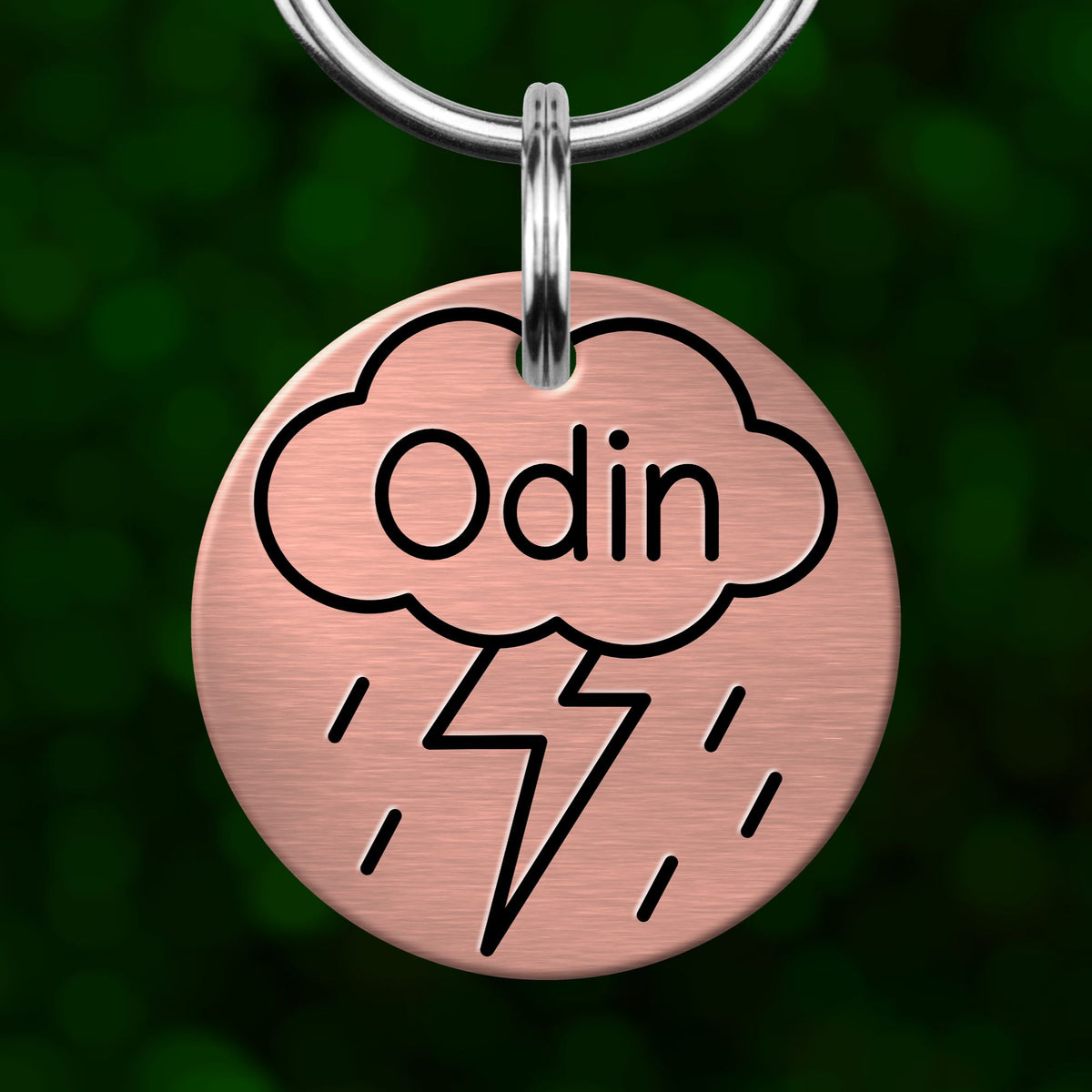 A round metal keychain tag with a cloud design and a lightning bolt symbol, with the word "Odin" written on it.