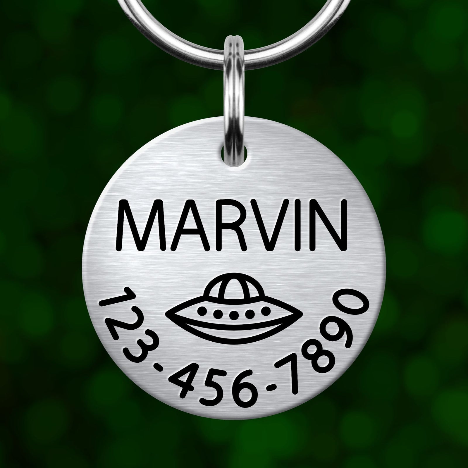 A silver metal pet tag with the name "MARVIN" and a graphic of an alien spacecraft.