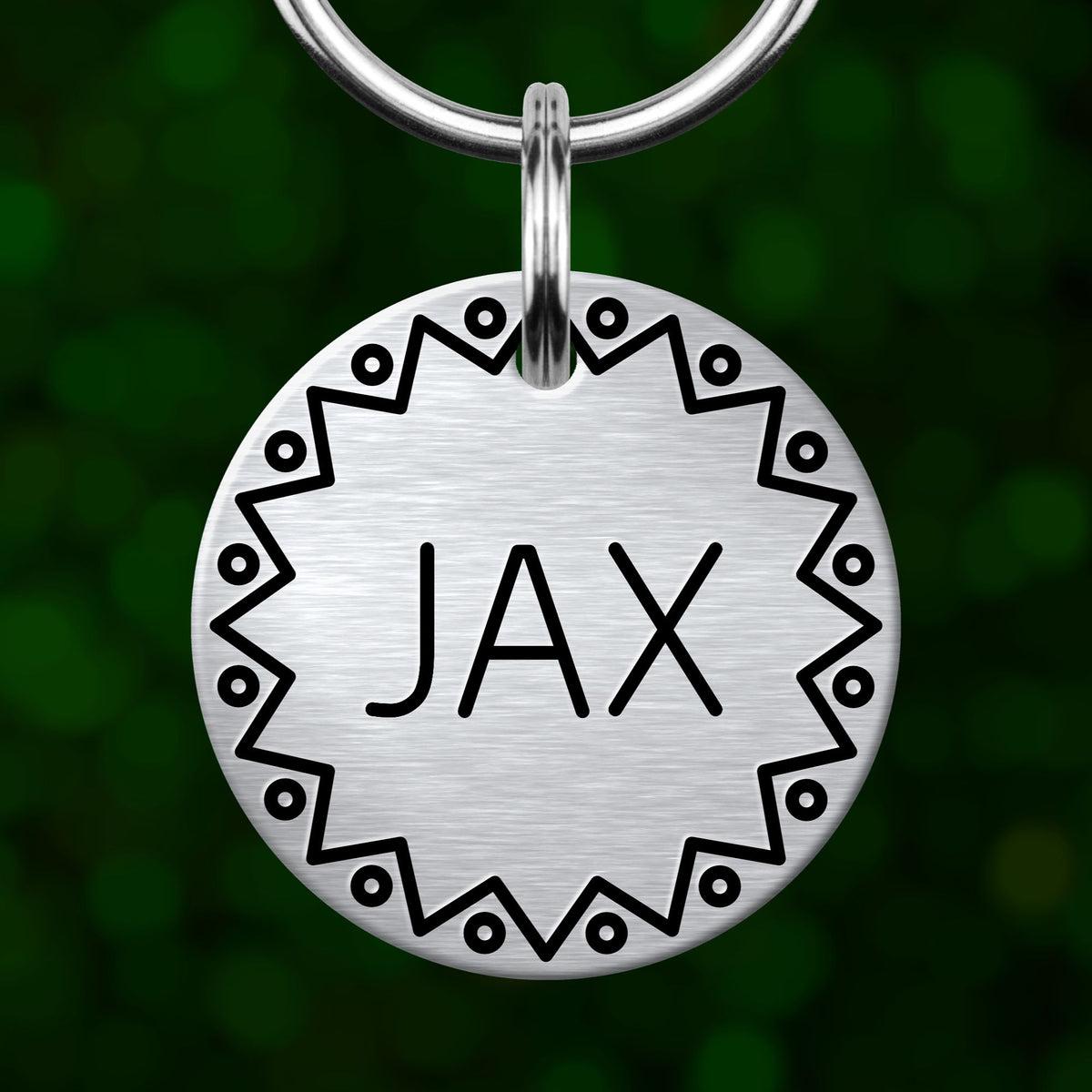 A silver metal pet tag with the name "JAX" engraved on it, hanging from a keychain.