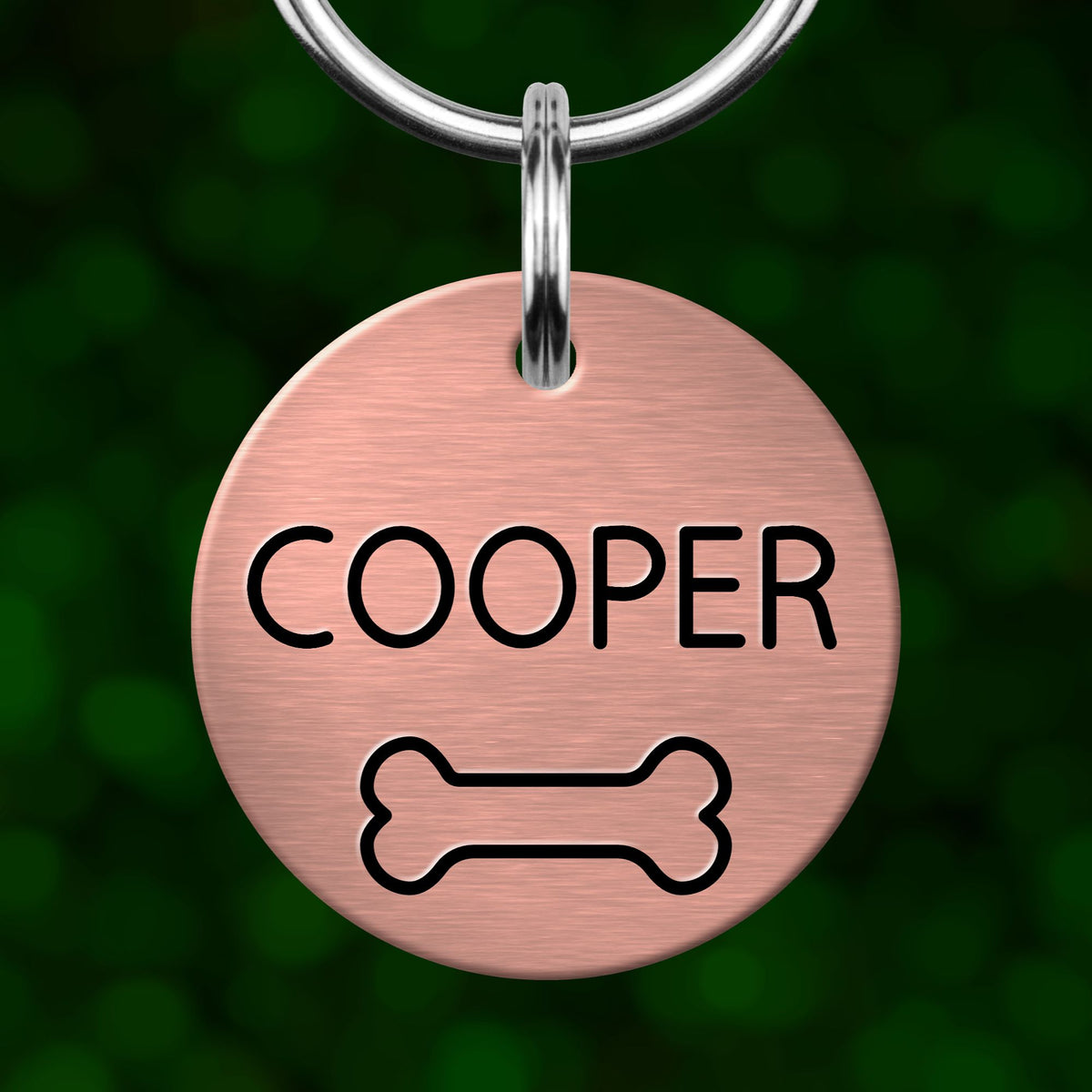 A round metal pet tag with the name "COOPER" printed on it, along with a bone symbol.