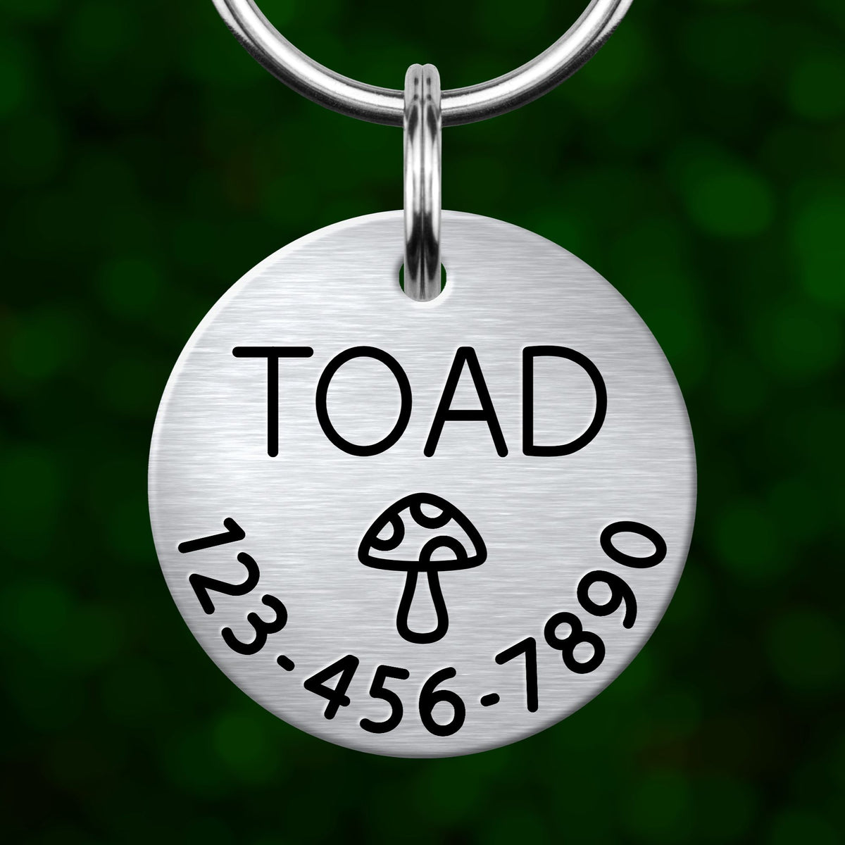 A silver-colored metal tag with the word "TOAD" printed on it, along with a mushroom icon and some numbers below it.