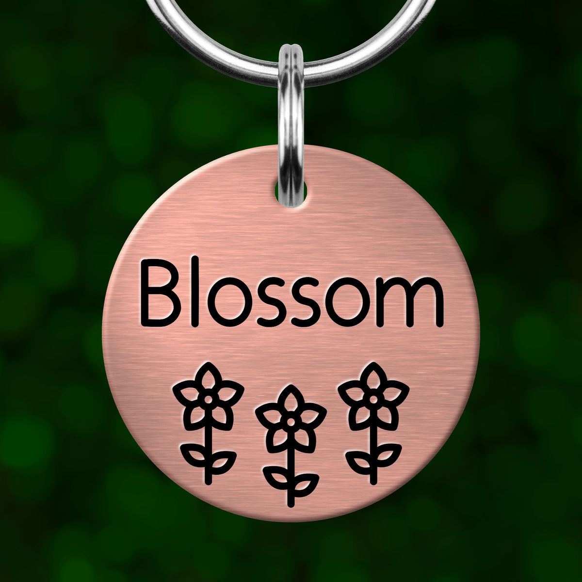 A round metal pet tag with the word "Blossom" written on it, along with three flower icons.